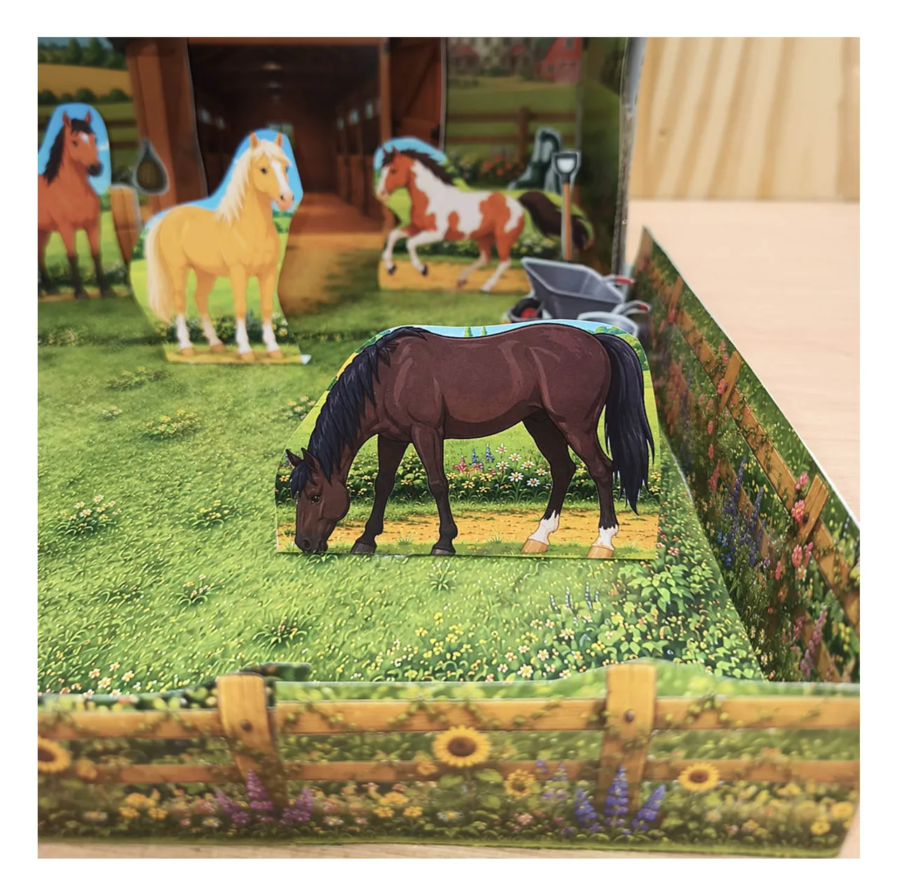 Paper horses standing in a grassy paddock with wooden flower fences and country scenery in a shoebox diorama