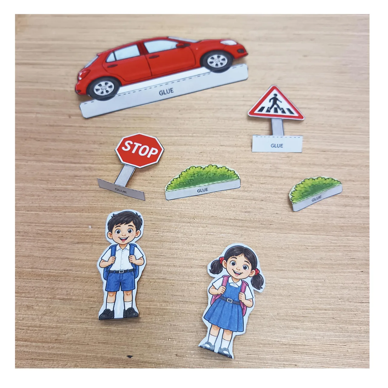 Paper cutouts of schoolchildren, a red car, a stop sign, a pedestrian crossing sign and bushes.