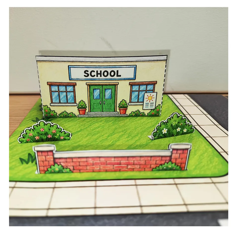 Paper school building on a green plot beside the pavement